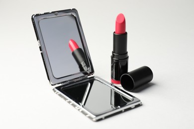 Photo of Open pocket mirror and lipstick on light grey background, closeup