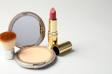 Photo of Open face powder with mirror, brush and lipstick on light grey background, closeup. Space for text