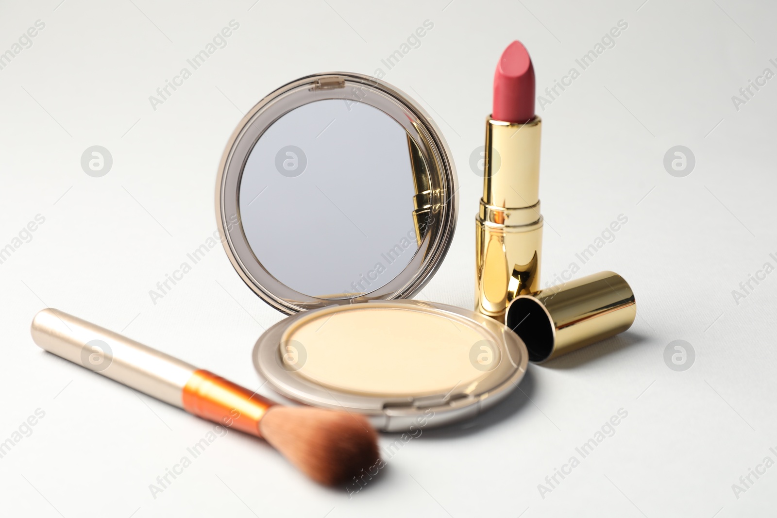Open face powder with mirror, brush and lipstick on light grey background, closeup Photo of Open face powder with mirror, brush and lipstick on light grey background, closeup