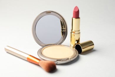 Photo of Open face powder with mirror, brush and lipstick on light grey background, closeup