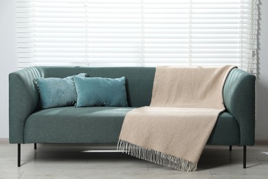 Photo of Woolen plaid and cushions on sofa at home