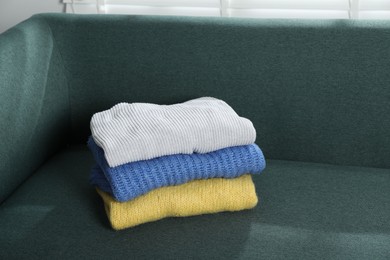 Photo of Stack of woolen sweaters on sofa indoors