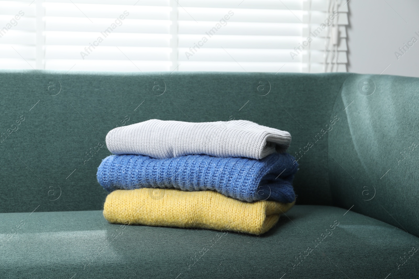 Stack of woolen sweaters on sofa indoors Photo of Stack of woolen sweaters on sofa indoors
