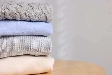 Photo of Stack of woolen sweaters on wooden table against light background, closeup. Space for text