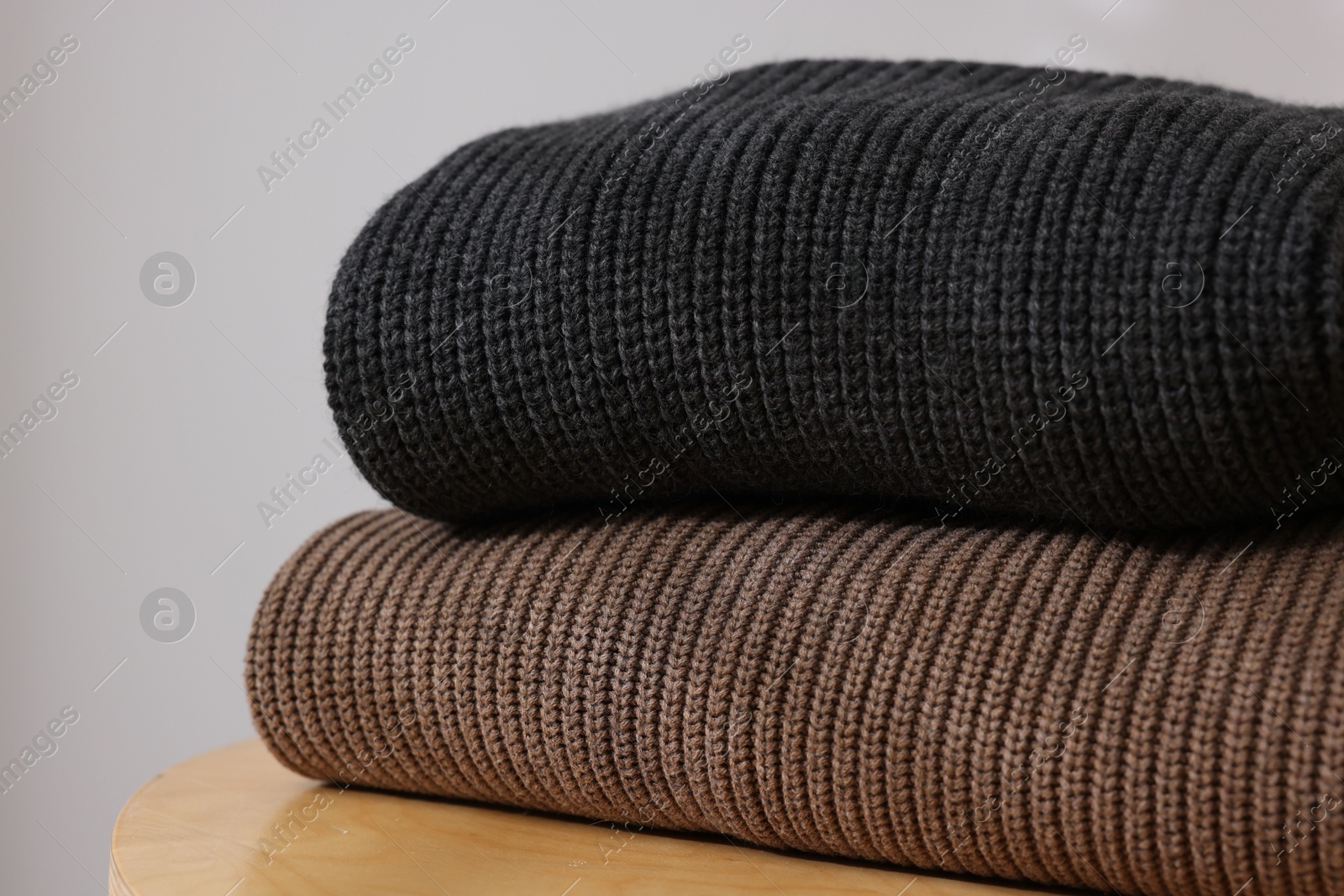 Stack of woolen sweaters on wooden table against light background, closeup Photo of Stack of woolen sweaters on wooden table against light background, closeup