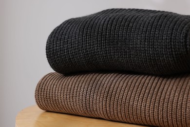 Photo of Stack of woolen sweaters on wooden table against light background, closeup