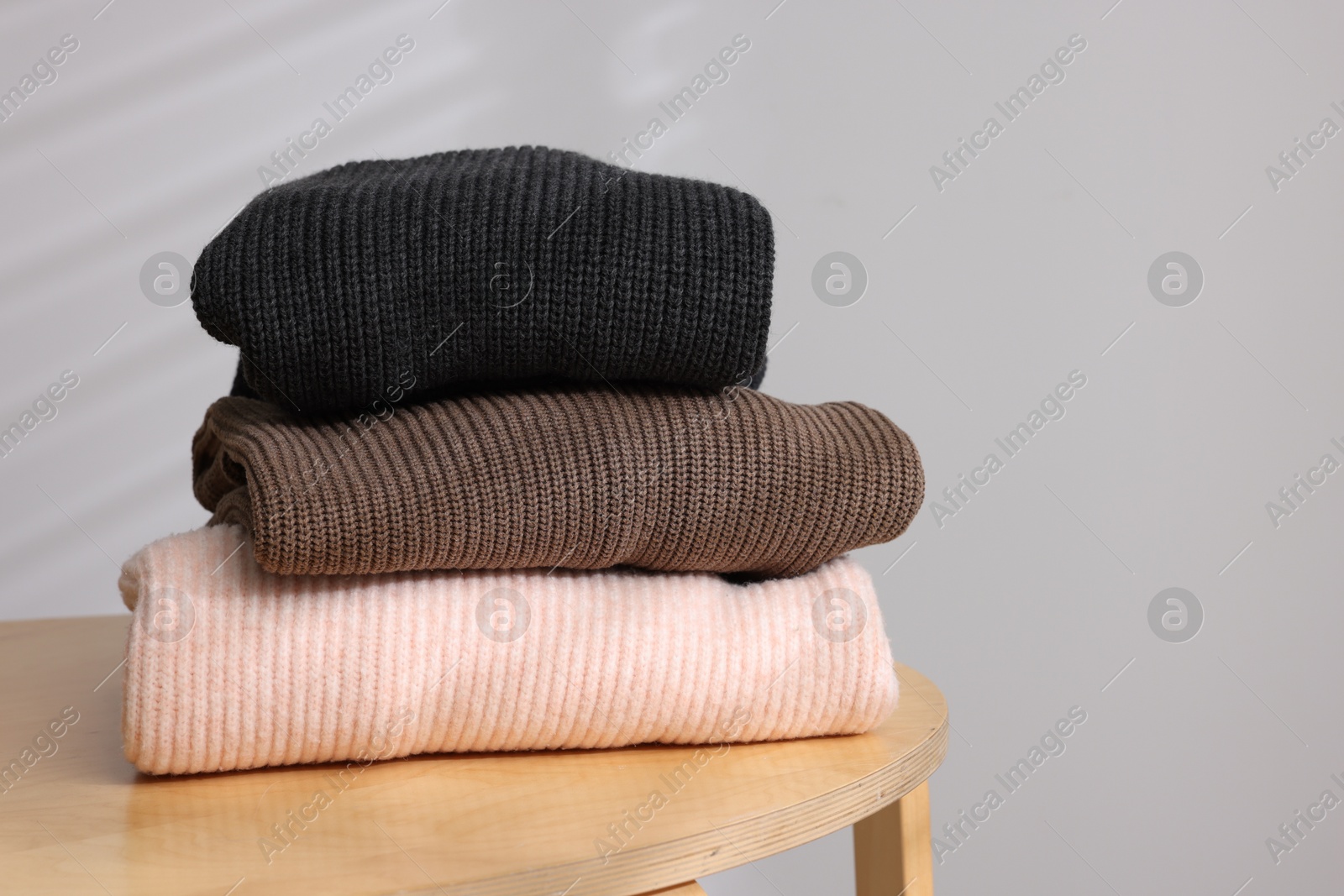 Stack of woolen sweaters on wooden table against light background. Space for text Photo of Stack of woolen sweaters on wooden table against light background. Space for text