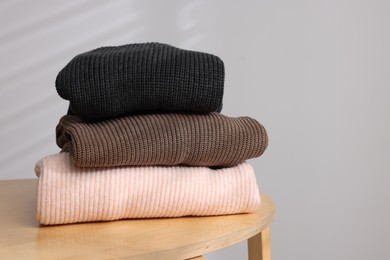 Photo of Stack of woolen sweaters on wooden table against light background. Space for text