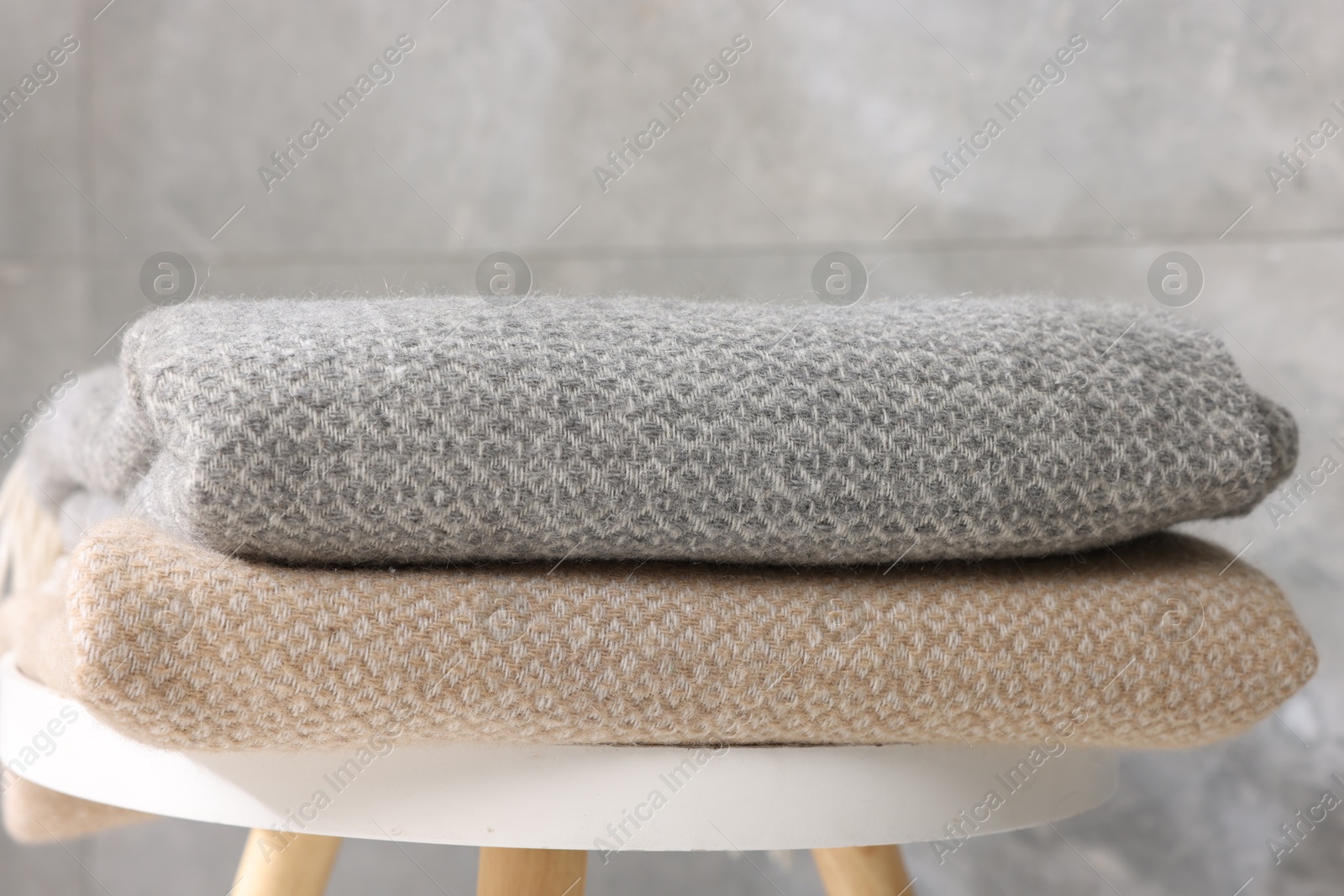 Folded woolen plaids on table near grey wall, closeup Photo of Folded woolen plaids on table near grey wall, closeup