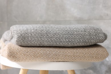 Photo of Folded woolen plaids on table near grey wall, closeup