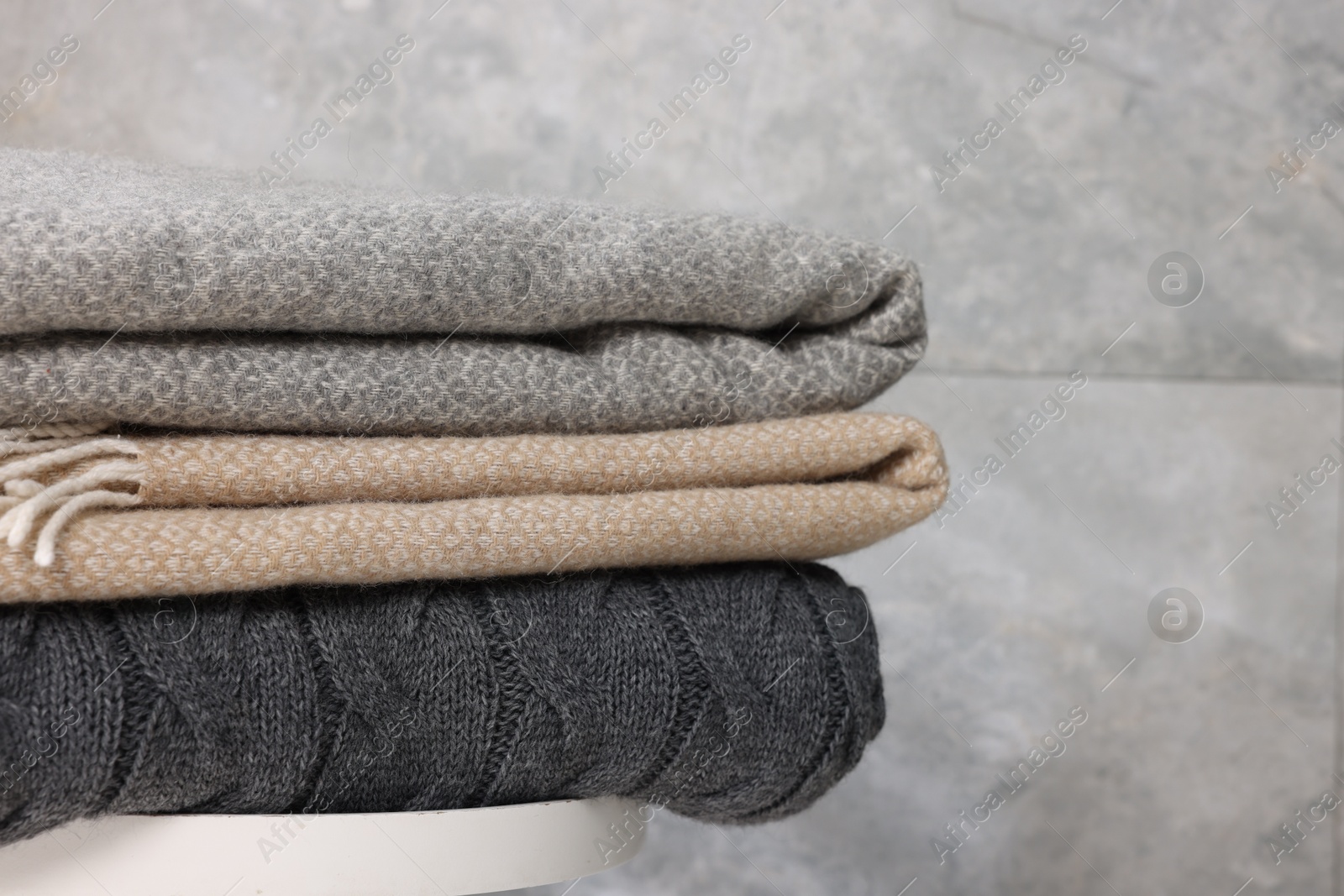 Folded woolen plaids on table near grey wall, closeup Photo of Folded woolen plaids on table near grey wall, closeup