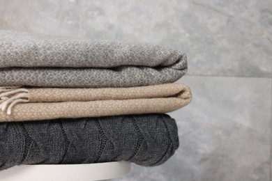 Photo of Folded woolen plaids on table near grey wall, closeup