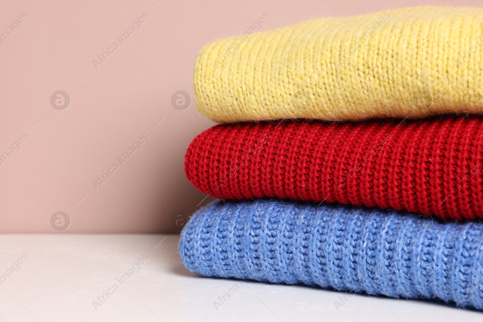 Stack of woolen sweaters on white table against color background, closeup. Space for text Photo of Stack of woolen sweaters on white table against color background, closeup. Space for text