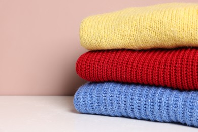 Photo of Stack of woolen sweaters on white table against color background, closeup. Space for text