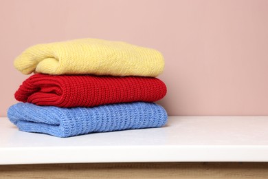 Photo of Stack of woolen sweaters on white table against color background. Space for text