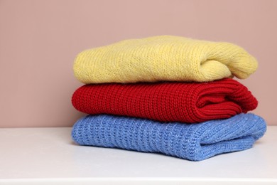 Photo of Stack of woolen sweaters on white table against color background, closeup