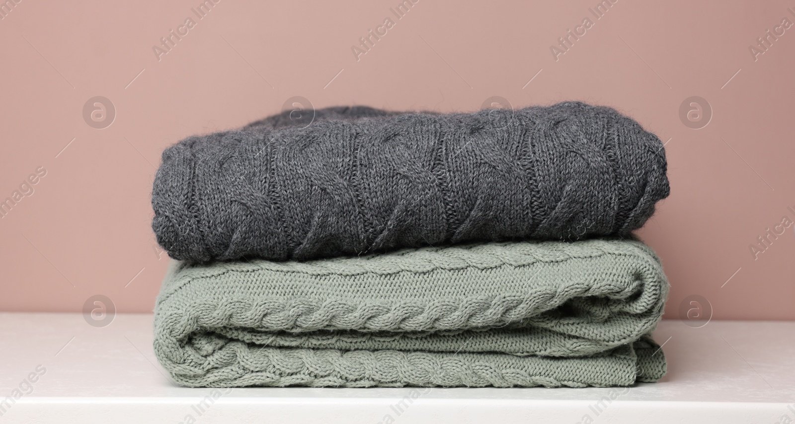Folded woolen plaids on white table against color background, closeup Photo of Folded woolen plaids on white table against color background, closeup