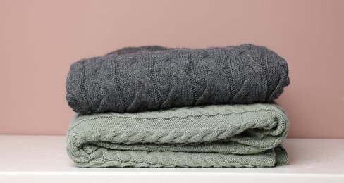 Photo of Folded woolen plaids on white table against color background, closeup