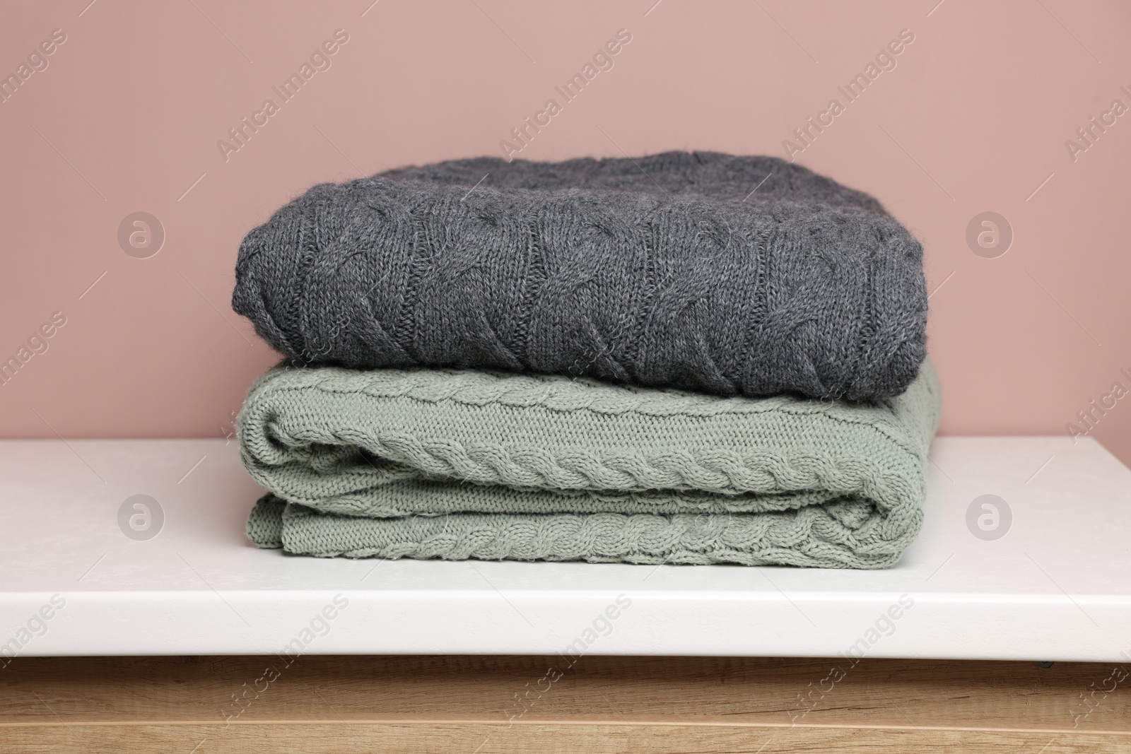 Folded woolen plaids on white table against color background, closeup Photo of Folded woolen plaids on white table against color background, closeup