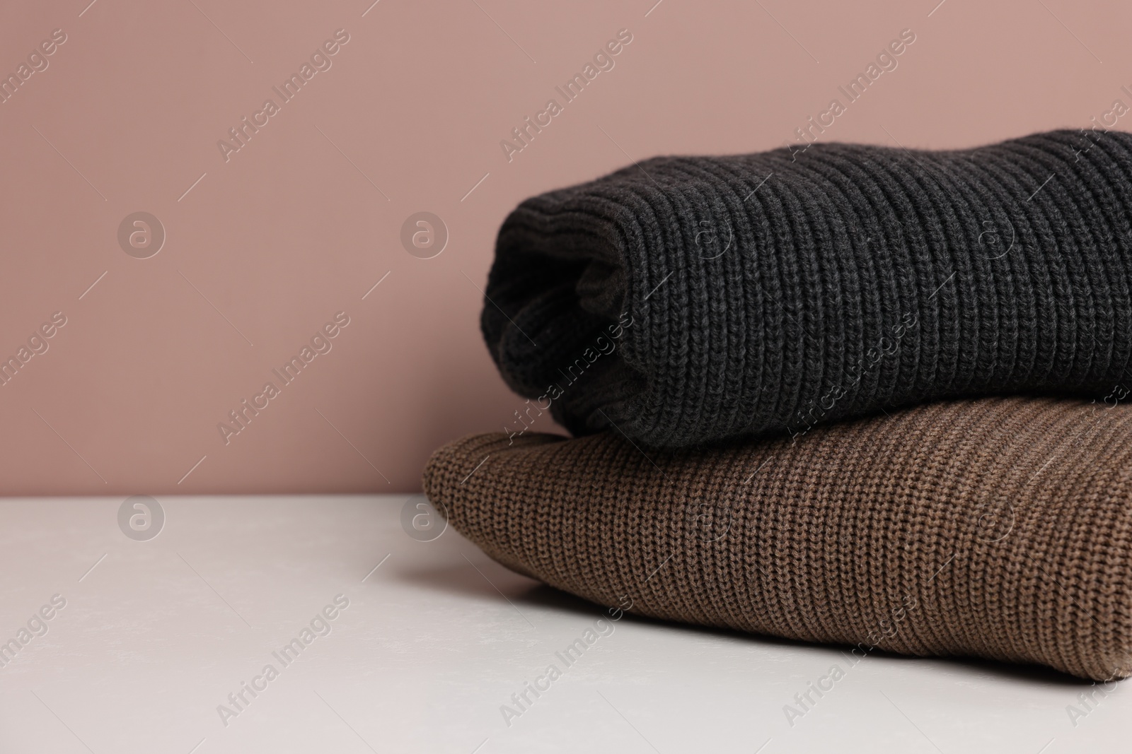 Photo of Stack of woolen sweaters on white table against color background, closeup. Space for text