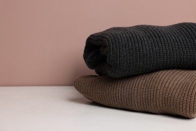 Photo of Stack of woolen sweaters on white table against color background, closeup. Space for text