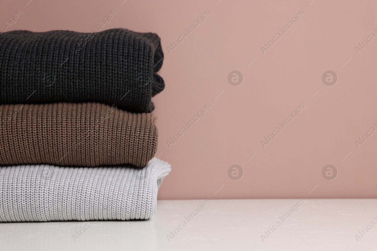 Photo of Stack of woolen sweaters on white table against color background, closeup. Space for text