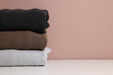 Photo of Stack of woolen sweaters on white table against color background, closeup. Space for text