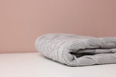 Photo of Folded woolen plaid on white table against color background, closeup. Space for text