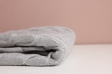 Photo of Folded woolen plaid on white table against color background, closeup. Space for text