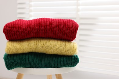 Photo of Stack of woolen sweaters on table near window, closeup