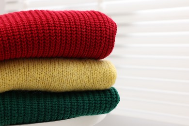 Photo of Stack of woolen sweaters on table near window, closeup