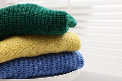 Photo of Stack of woolen sweaters on table near window, closeup