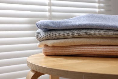 Photo of Stack of woolen sweaters on wooden table near window, closeup