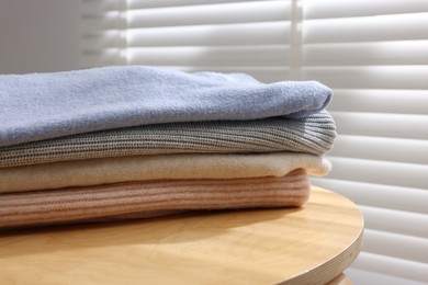 Photo of Stack of woolen sweaters on wooden table near window, closeup