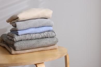 Photo of Stack of woolen sweaters on wooden table against light background. Space for text