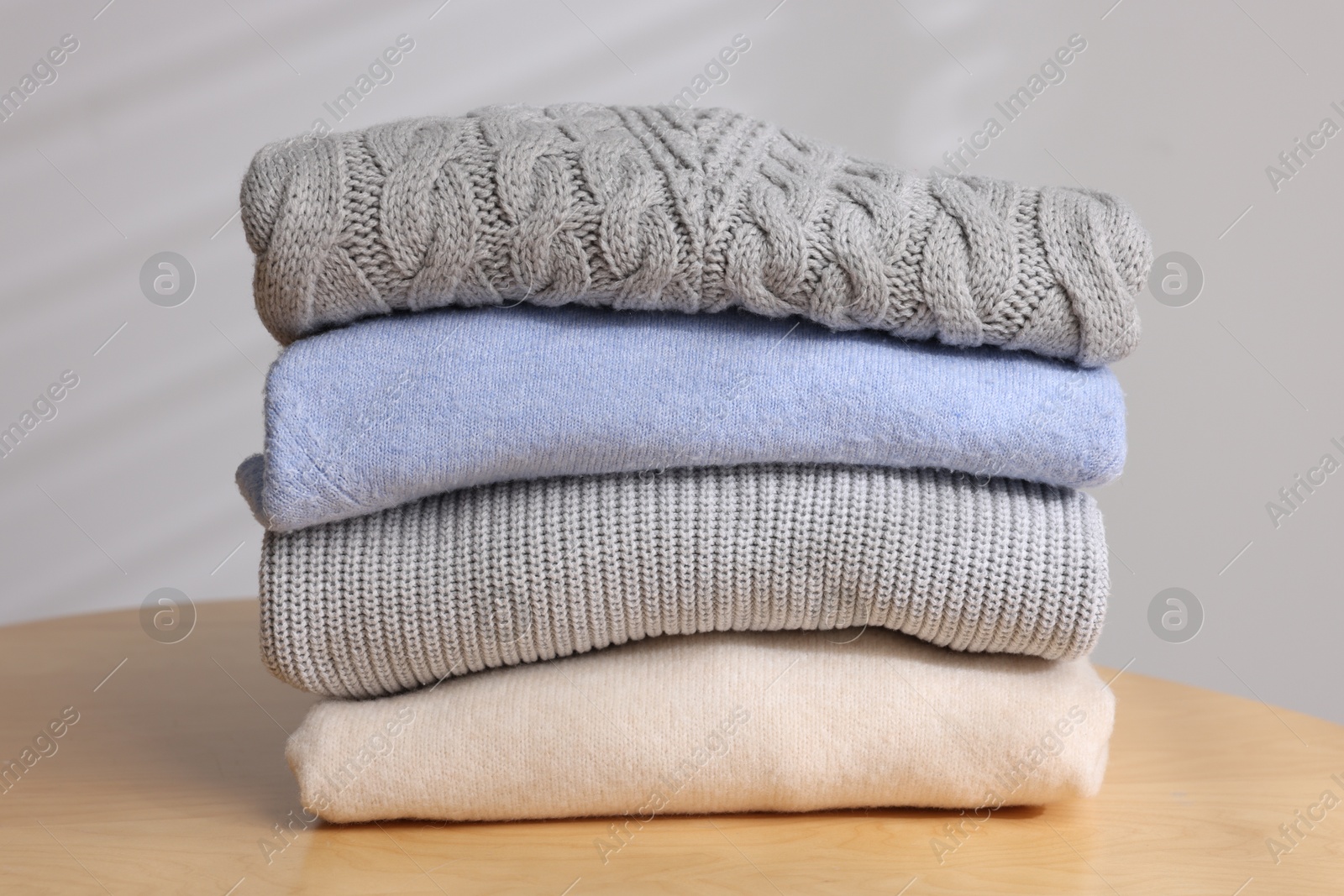 Stack of woolen sweaters on wooden table against light background, closeup Photo of Stack of woolen sweaters on wooden table against light background, closeup