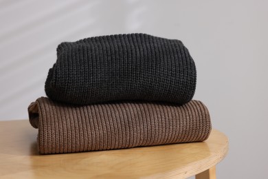 Photo of Stack of woolen sweaters on wooden table against light background, closeup