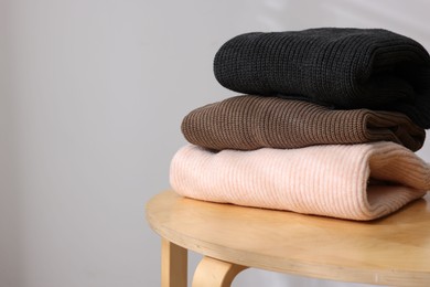 Photo of Stack of woolen sweaters on wooden table against light background, closeup. Space for text