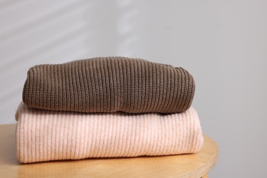 Photo of Stack of woolen sweaters on wooden table against light background, closeup