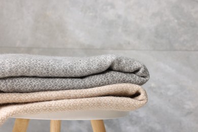 Photo of Folded woolen plaids on table near grey wall, closeup