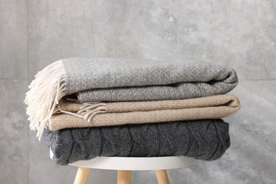 Photo of Folded woolen plaids on table near grey wall, closeup