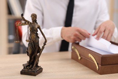 Photo of Judge working and Lady Justice figure on desk indoors, selective focus
