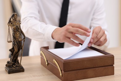 Photo of Judge working and Lady Justice figure on desk indoors, selective focus
