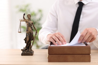 Photo of Judge working and Lady Justice figure on desk indoors, selective focus