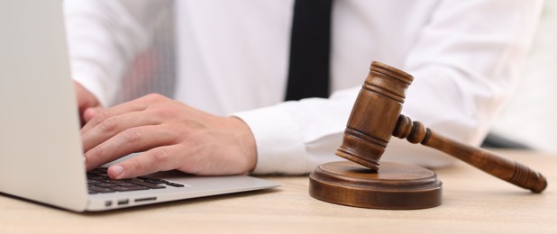 Photo of Judge working with laptop and gavel at desk indoors, closeup