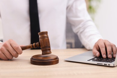 Photo of Judge working with laptop and gavel at desk indoors, closeup