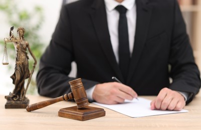 Photo of Judge working, Lady Justice figure and gavel on desk indoors, selective focus