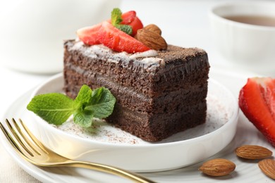 Photo of Piece of delicious chocolate cake with strawberry, almonds and mint on table, closeup