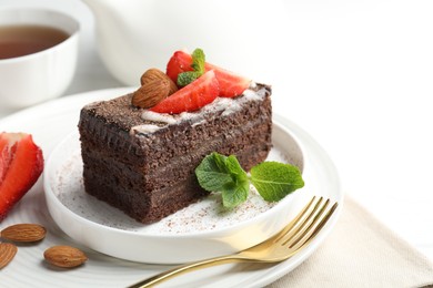 Photo of Piece of delicious chocolate cake with strawberries, almonds, mint and tea on table, closeup