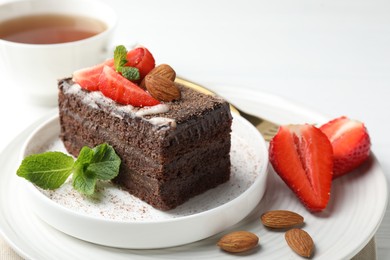Photo of Piece of delicious chocolate cake with strawberries, almonds, mint and tea on table, closeup